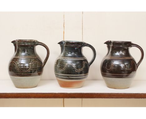 Winchcombe Pottery: three stoneware studio pottery jugs - of matching baluster form, in various glazes, all with waved line a