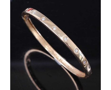 A yellow metal diamond oval hinged bangle, comprising seven round brilliant cut diamonds in flush settings, with a box clasp,