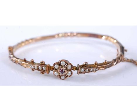 A yellow metal hinged hollow twist bangle, having a central flower cluster with six 2.1mm seed pearls and five graduated 1.6 