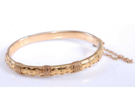 A yelllow metal Etruscan style oval hinged hollow bangle, with box clasp and safety chain, bangle width 6.15mm, inner diamete