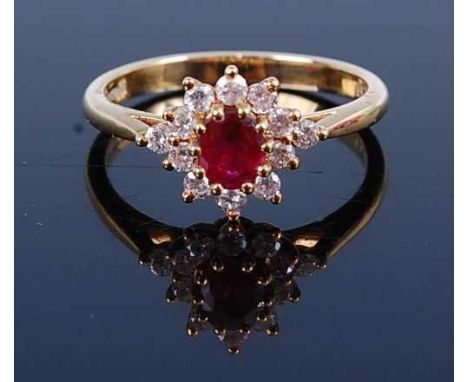 An 18ct gold, ruby and diamond flower head cluster ring, the oval cut ruby weighing approx 0.5 carats, within a surround of t