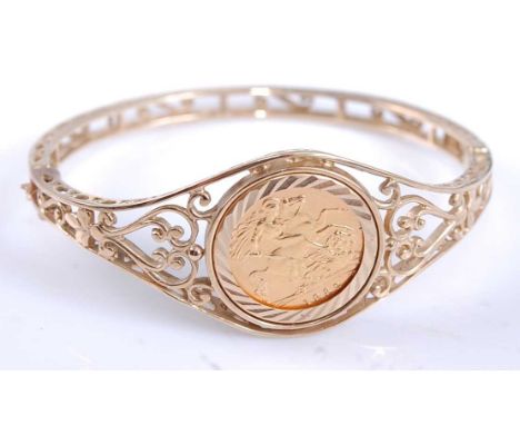 A Queen Elizabeth II 1982 half sovereign within a yellow metal open scrollwork hinged bangle, with box clasp and figure of ei