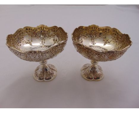 A pair of silver pedestal bowls chased with flowers and leaves on raised circular lobed feet, London 1907 by Henry Wilkinson 