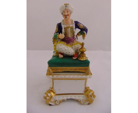 An early 19th century Royal Crown Derby figurine of an Arabian gentleman seated on a pillow mounted on a square architectural