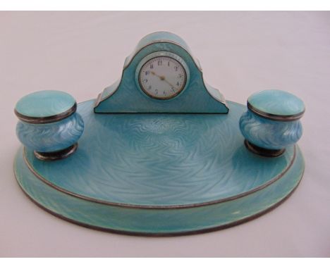 A silver and enamel ink stand of oval form with two vase form inkwells with hinged covers and an integral desk clock, circa 1