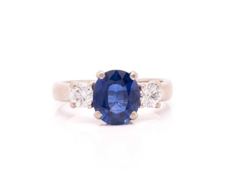 A three-stone sapphire and diamond ring in 18ct white gold, set to the centre with an oval-cut sapphire of bright blue colour