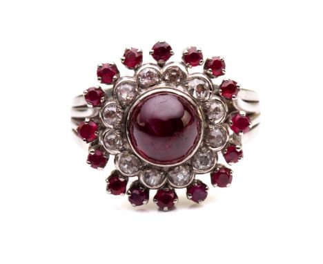 A cabochon ruby and diamond cluster ring; the central, circular ruby in collet mount above a border of mixed old cut diamonds