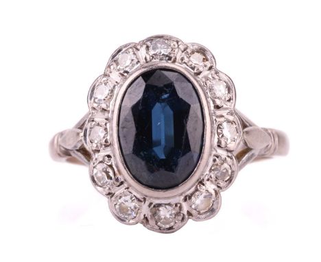 A sapphire and diamond entourage ring, centred with an oval-cut sapphire of dark greenish-blue colour, approximately measures