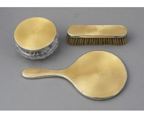 A three piece guilloche enamel dressing table set, in pale yellow, London 1955, comprising hand mirror, brush and powder jar 