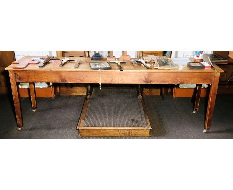 An early 20th Century grain varnished pine farmhouse table, single rectangular top above a frieze shelf, raised on block tape