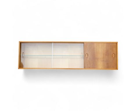 A walnut wall cabinet by Heals - rectangular with a solid sliding section with two glazed slides enclosing a shelf, 136 x 24 
