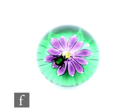 A contemporary William Manson glass paperweight of domed form, internally decorated with a stylised mauve lamp work flower wi
