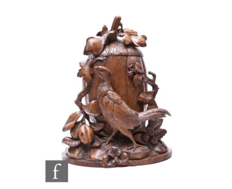 A late 19th Century walnut Black Forest tobacco jar and cover, carved with a pheasant amidst fruit and foliage below an oak l