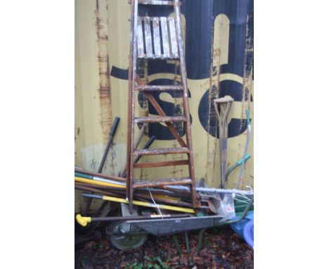 A WHEELBARROW CONTAINING GARDEN TOOLS and a vintage wooden step ladder