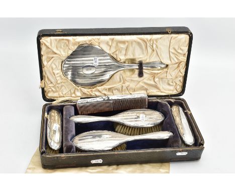 A SIX PIECE SILVER VANITY TRAVEL SET, comprising of a circular mirror, hair brush and clothes brush all within an engine turn