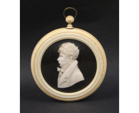 An early 19th Century carved ivory portrait roundel, head and shoulders of a young man with well carved curled hair, on a bla