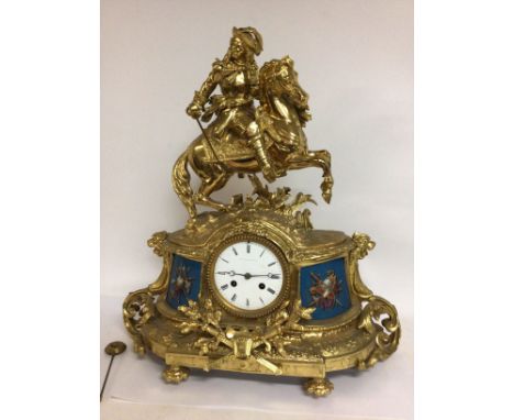 A gilt metal manual clock the top surmounted with a cavalier the dial With Roman numerals flanked by painted metal panels. No