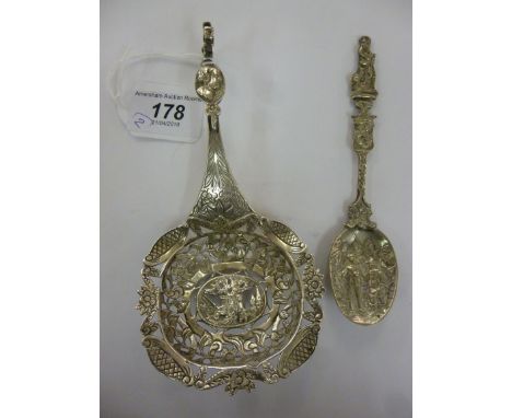 A Continental silver coloured metal presentation sifter spoon, ornamented to the centre with figures, bordered by foliage and