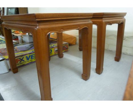 A pair of modern Chinese light coloured hardwood occasional tables, each having a panelled top, over a scrolled apron, raised