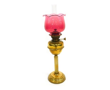 A late 19th/early 20thC brass oil lamp, with a cranberry glass shade, brass central reservoir, a Corinthian column, on a step
