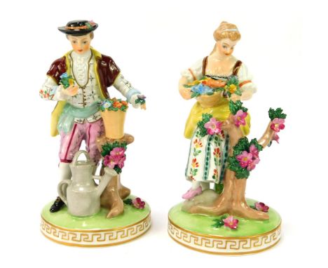 A pair 20thC Dresden porcelain figures, modelled as gardeners, the female holding a basket of flowers leaning against a tree 