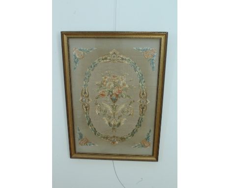 An early 20th Century embroidered silk panel, depicting a stylized urn with flowers, above flamboyant foliate scrolls, on a m
