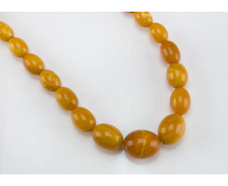 An Art Deco period amber bead necklace, having a single knotted string of toffee and caramel coloured oval prehistoric amber 