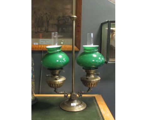 A brass patent twin light oil lamp, with Royal coat of arms to the central boss, and green overlaid milk glass shades, 64cm h