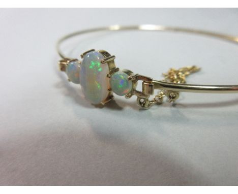 A three stone opal bangle, set to the front with a long oval between two round cabochon opals on a fixed base with open squar