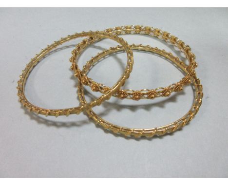 Three precious yellow metal bangles, testing for very high carat, two of the bangles designed as a textured band wrapped arou
