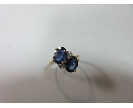 A sapphire, diamond and 18ct gold crossover ring, obliquely set with two oval cut mid-blue sapphires and two round brilliant 