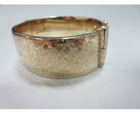 A 9ct gold hinged bangle, the 2.5cm wide bangle with bright cut foliate decoration to the front and engraved dedication insid