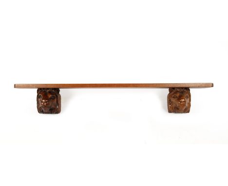 Carved lion shelfoak, each end supported by carved lion masks, the shelf with canted corners, 122cm wide x 17cm deep x 18cm h
