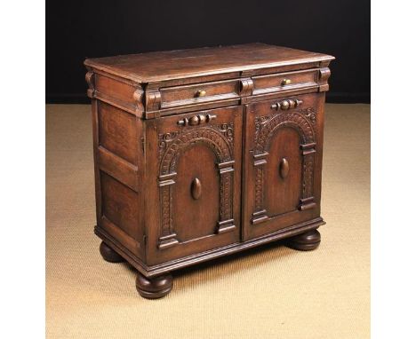 A 17th Century Oak Cupboard housing a moulded frieze drawer with oval brass knop handles above arched panel doors carved with