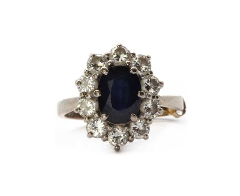 An 18ct white gold sapphire and diamond cluster ring, an oval mixed cut sapphire, approximately 8.25 x 6.25mm, to surround of