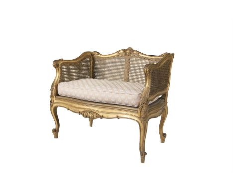 A SMALL GILTWOOD FRAMED BERGERE SEAT WITH LOOSE SQUAB CUSHION, the crest rail with foliate scroll, the armrests with leaf scr