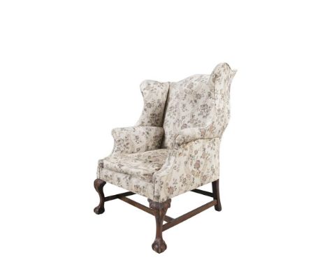 A GEORGIAN STYLE MAHOGANY WING BACK ARMCHAIR OF GENEROUS PROPORTIONS COVERED IN FLORAL TAPESTRY STYLE CLOTH, raised on carved