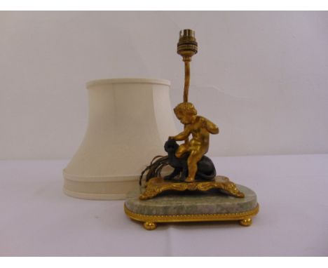 An early 20th century gilt metal and marble table lamp with a cast figurine of a putti fighting a lion, to include a silk sha