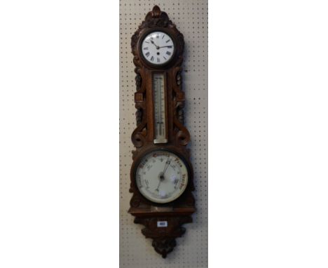 A late Victorian ornate carved and pierced oak framed wall barometer/thermometer with aneroid works and timepiece movement to