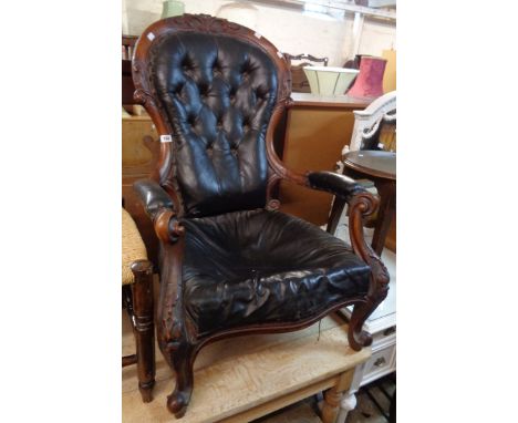 A Victorian carved walnut show frame gentleman's drawing room armchair with remains of button back rexine upholstery, set on 