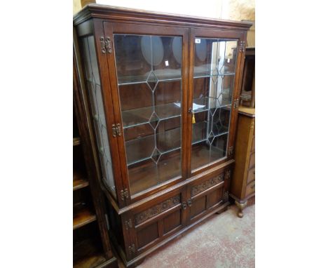 A 3' 6 1/2" Old Charm stained oak display cabinet with glass shelves enclosed by a pair of leaded glazed panel doors, over de