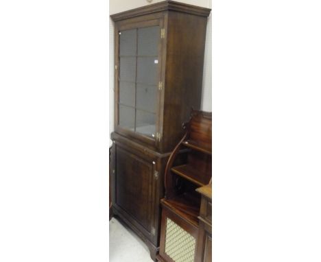 An oak cupboard in the 19th Century manner, the moulded cornice above a single glazed door opening to reveal shelving over a 