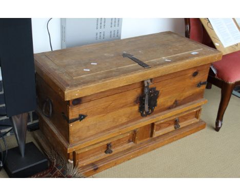 A pine trunk with metal mounts, the rectangular top above two drawers, on a plinth base