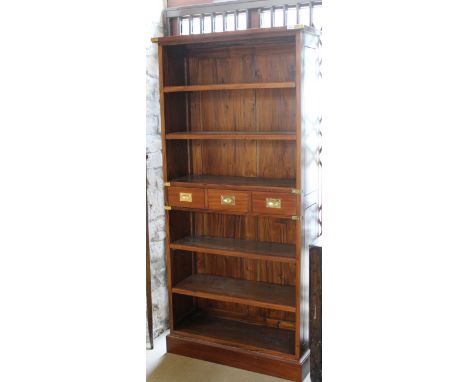 A modern mahogany six shelf open bookcase and three short drawers with campaign style handles, raised on a plinth base