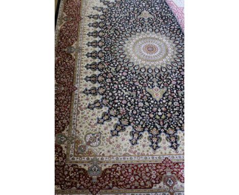 A Persian rug with central wheel pattern in white, sage green, reds, pinks, yellow and cream on a midnight blue ground, with 