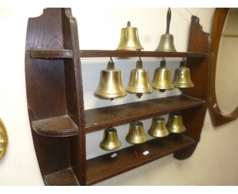 AN EARLY 20TH CENTURY BUTLER'S BELLS, on an oak wall shelf, comprising of nine various bells and another bell together with a