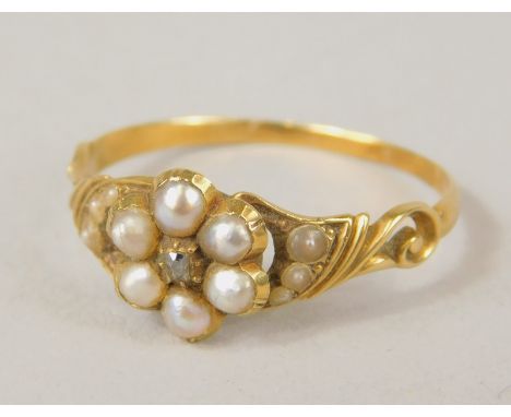 An early 20thC ladies dress ring, florally set with seed pearls on an elaborate part pierced scroll shank, unmarked