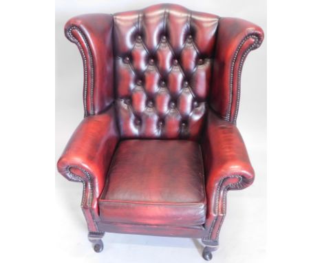 A modern club red leather style wing armchair, with beaded outline, button back, and compressed inverted front club supports,