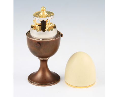 A silver and enamel egg cup by Anthony Elson, the removable egg cover revealing a gilt clockwork merry-go-round, numbered '20