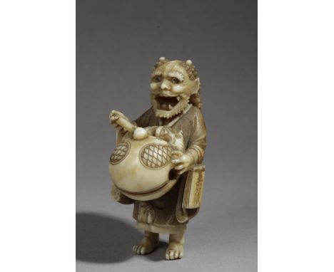 A late 19th century Japanese netsuke in carved ivory portraying a standing demon with mother of pearl inlaid eyes, flaunting 